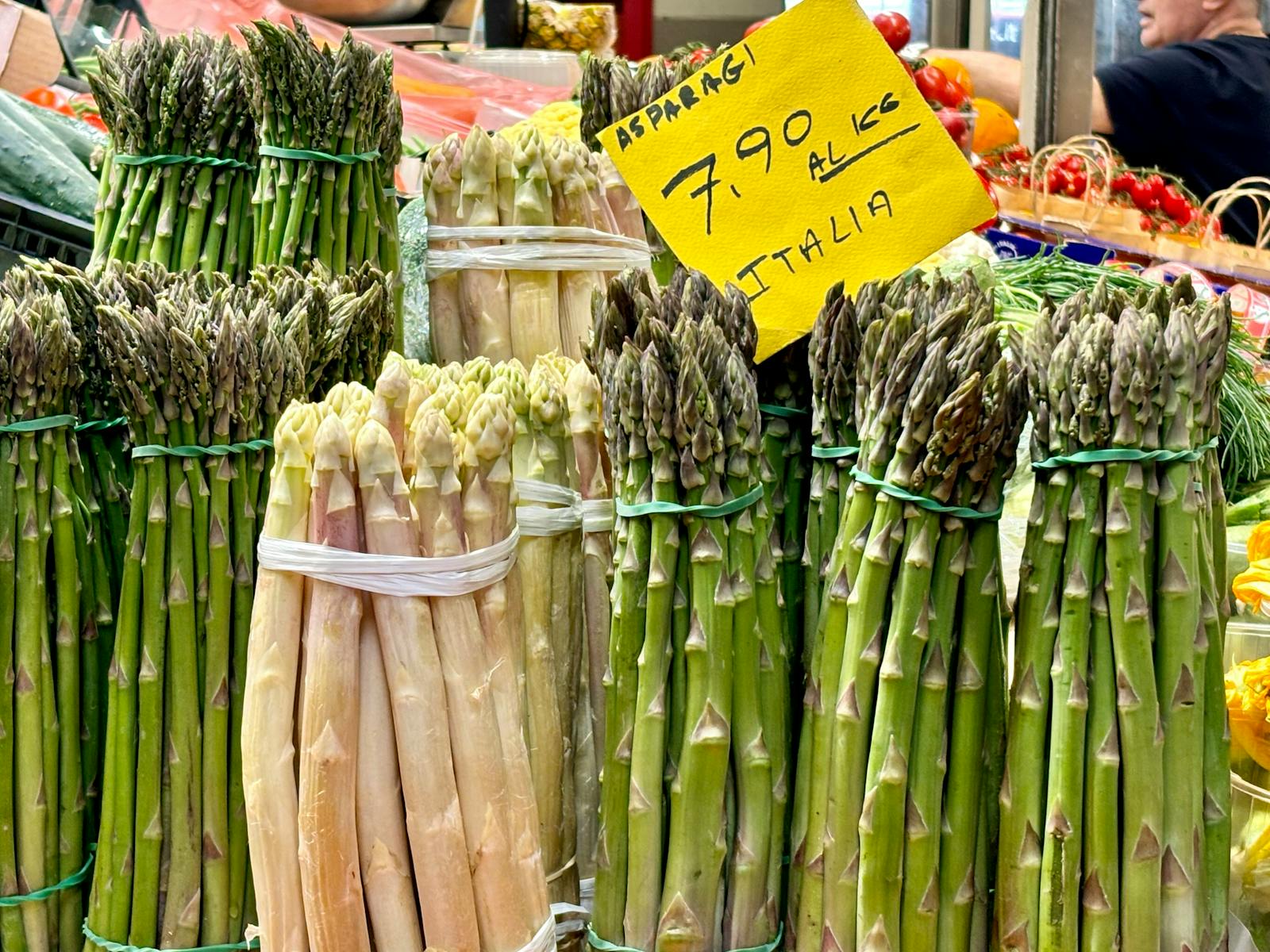 Bundles of fresh green and white asparagus stacked at a farmers market stall