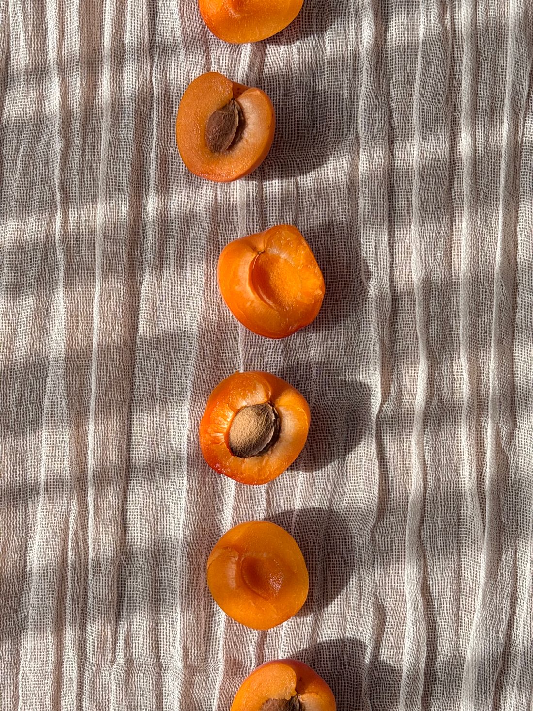 Fresh apricots halved to reveal their pits, arranged on a linen cloth